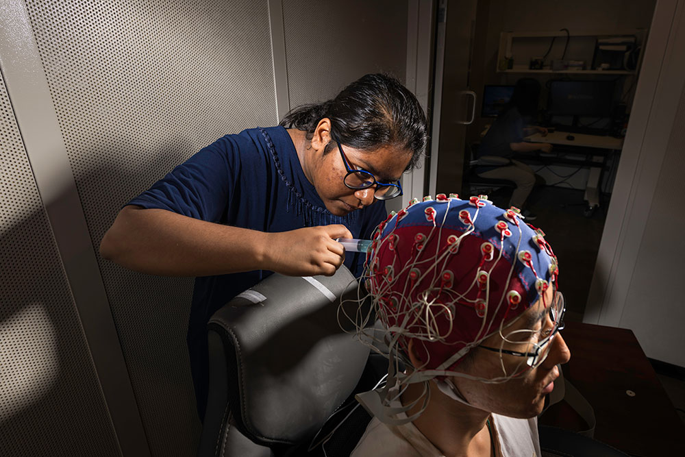 A student adjusting a brain mapping cap on another student.